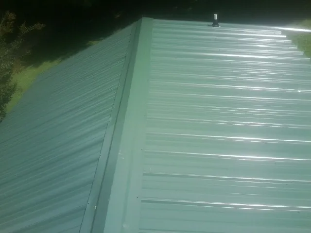 New green metal panels meeting at the ridge of a roof — Flat Roof Repair work by our crew in Portsmouth